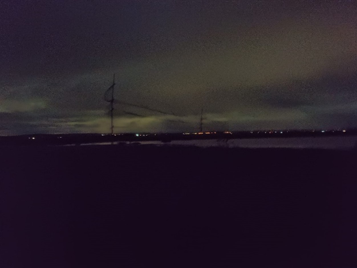 a night time scene showing a fine net cast high above the marshes with lights in the background